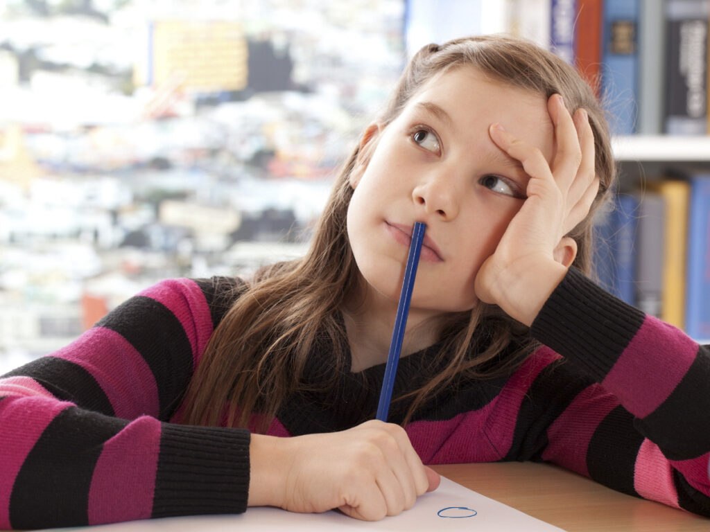 Mädchen sitzt mit Stift vor einem Blatt Papier und stützt den Kopf in die Hand